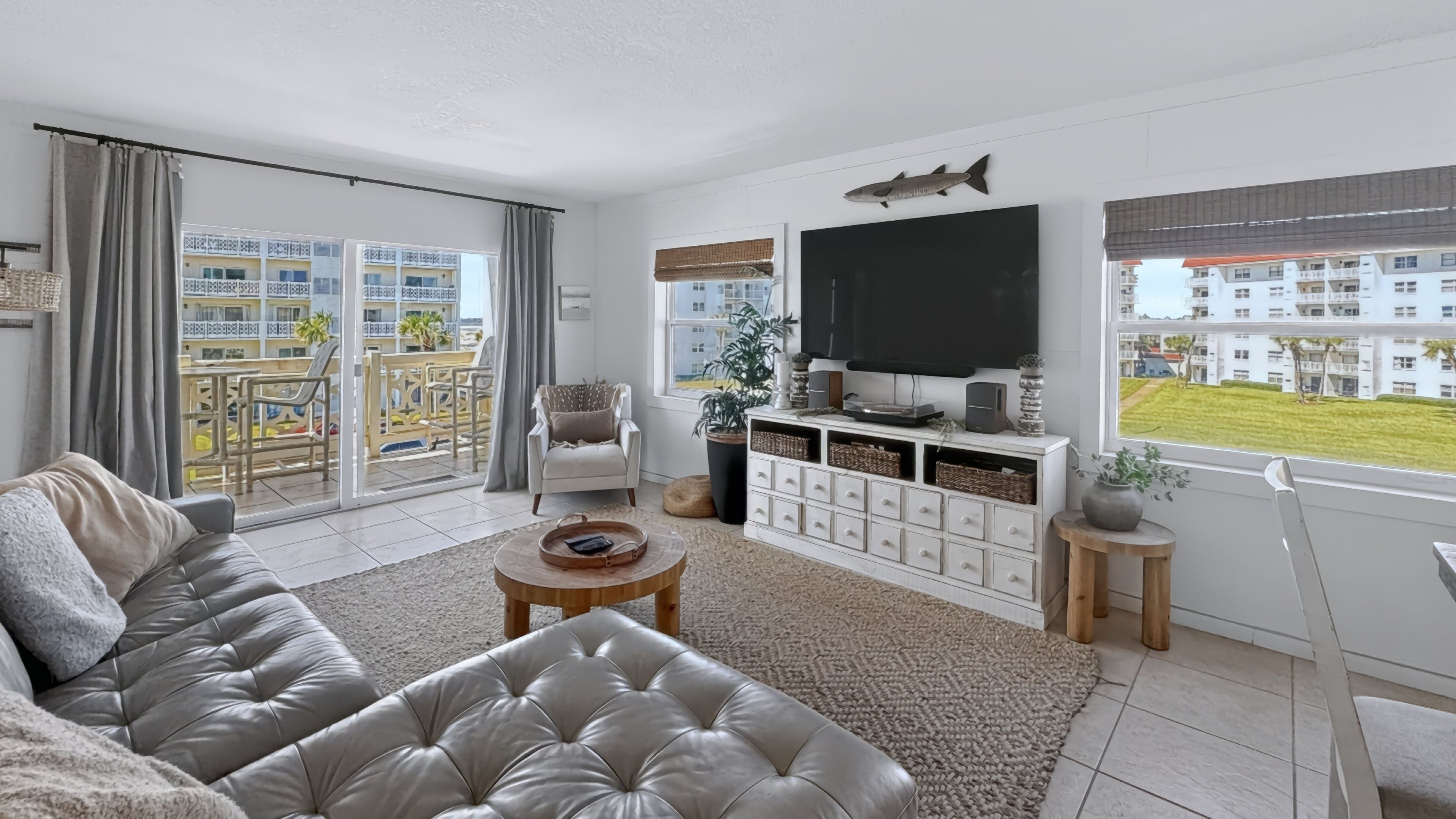 Un salon moderne avec un canapé en cuir, une table basse, un téléviseur et une vue sur un quartier résidentiel.