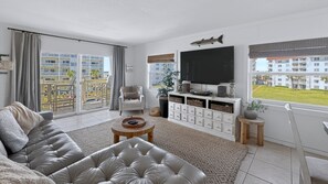 A modern living room with a leather sofa, a coffee table, a TV, and a view of a residential area.