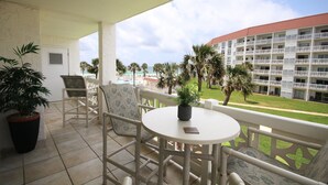 Un balcon avec une table et des chaises, un pot de fleurs et une vue sur un immeuble avec un toit rouge et des palmiers.
