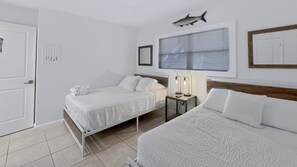 A hotel room with two beds, a desk, a lamp, a framed picture, and a fish mounted on the wall.