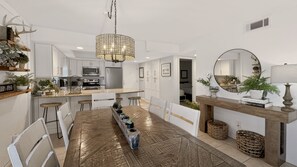 A modern kitchen with white cabinetry, a central island, and a dining area with a wooden table and white chairs. - El Matador 339 -  FREE TICKETS!! Your stay includes free tickets to many area attractions! (Fort Walton Beach)
