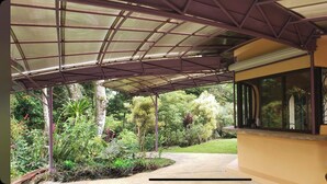 Un espacio al aire libre techado con metal, una ventana y un sendero que conduce a un jardín.