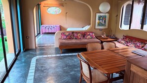 Una habitación acogedora con un sofá, una mesa de comedor y sillas. Se ve un ventanal con vistas a zonas verdes.