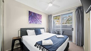 Une chambre à coucher avec un lit, un ventilateur de plafond, un tableau, une fenêtre avec des rideaux et une vue sur l’extérieur.