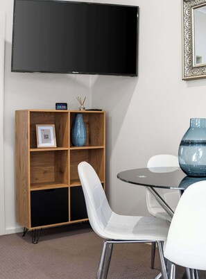 A modern room with a wooden cabinet, a glass table, white chairs, and a flat-screen TV mounted on the wall. - Prickly Pear Stays in Mayfield (Mayfield)