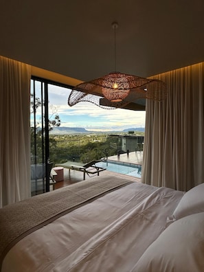 Relax in this serene bedroom with a large bed against a wall, featuring a window with a view of the pool and surrounding mountains.