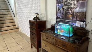 Quarto com piso de azulejos, cômoda de madeira, um pôster na parede e escada ao fundo.