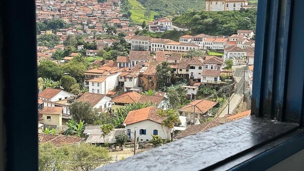 Vista da janela sobre uma cidade em encosta densamente povoada, com uma igreja imponente.