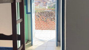 Um corredor estreito que dá para uma varanda com piso de azulejos e vista de edifícios ao longe.