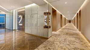 A modern hotel corridor with a marble floor, a large wall with vertical lines, and a digital elevator display. - Golden Tulip Kin-Oasis Kinshasa (Kinshasa)