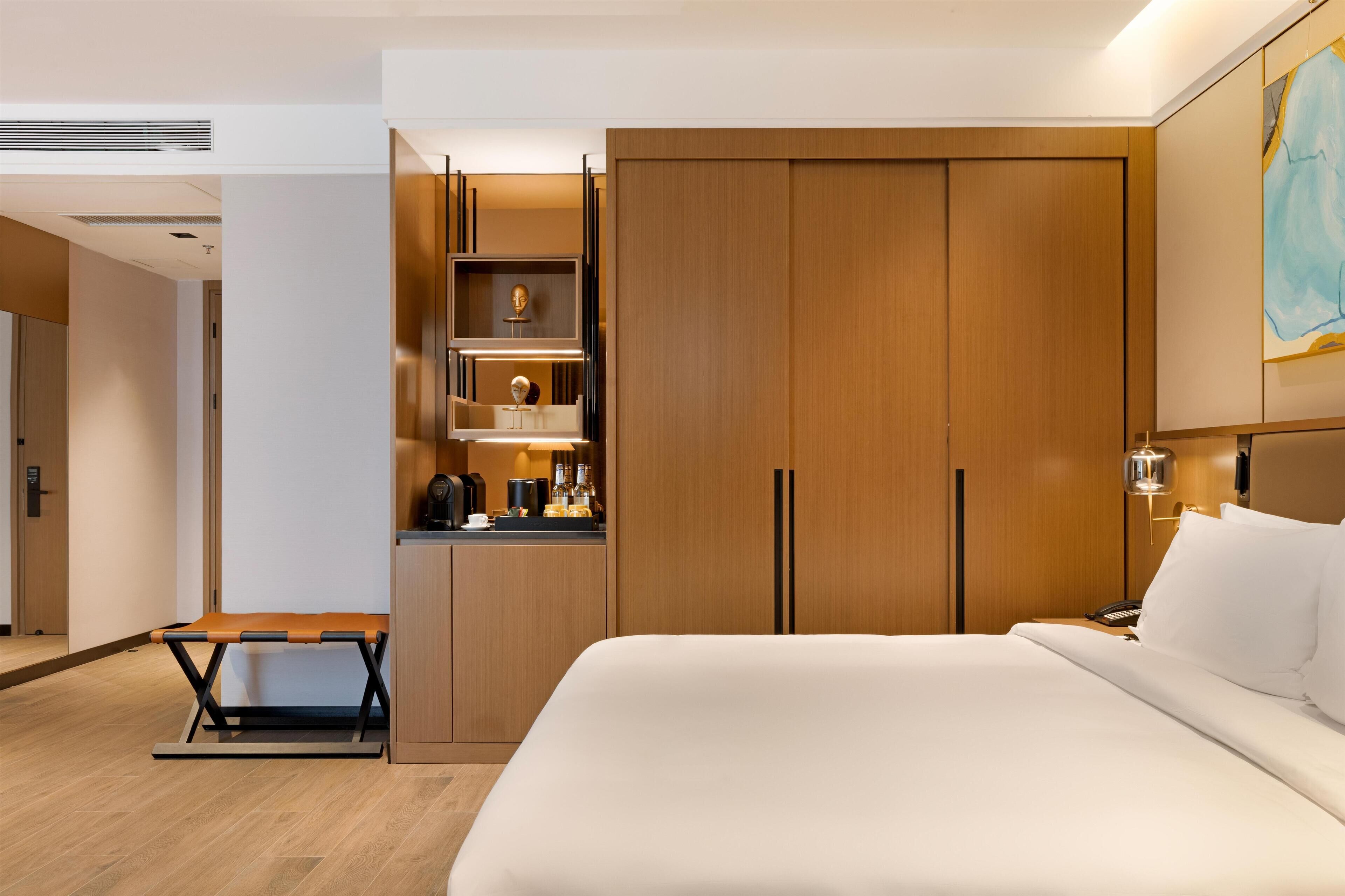 Une chambre d’hôtel moderne avec un grand lit, une armoire en bois et un petit coin cuisine.