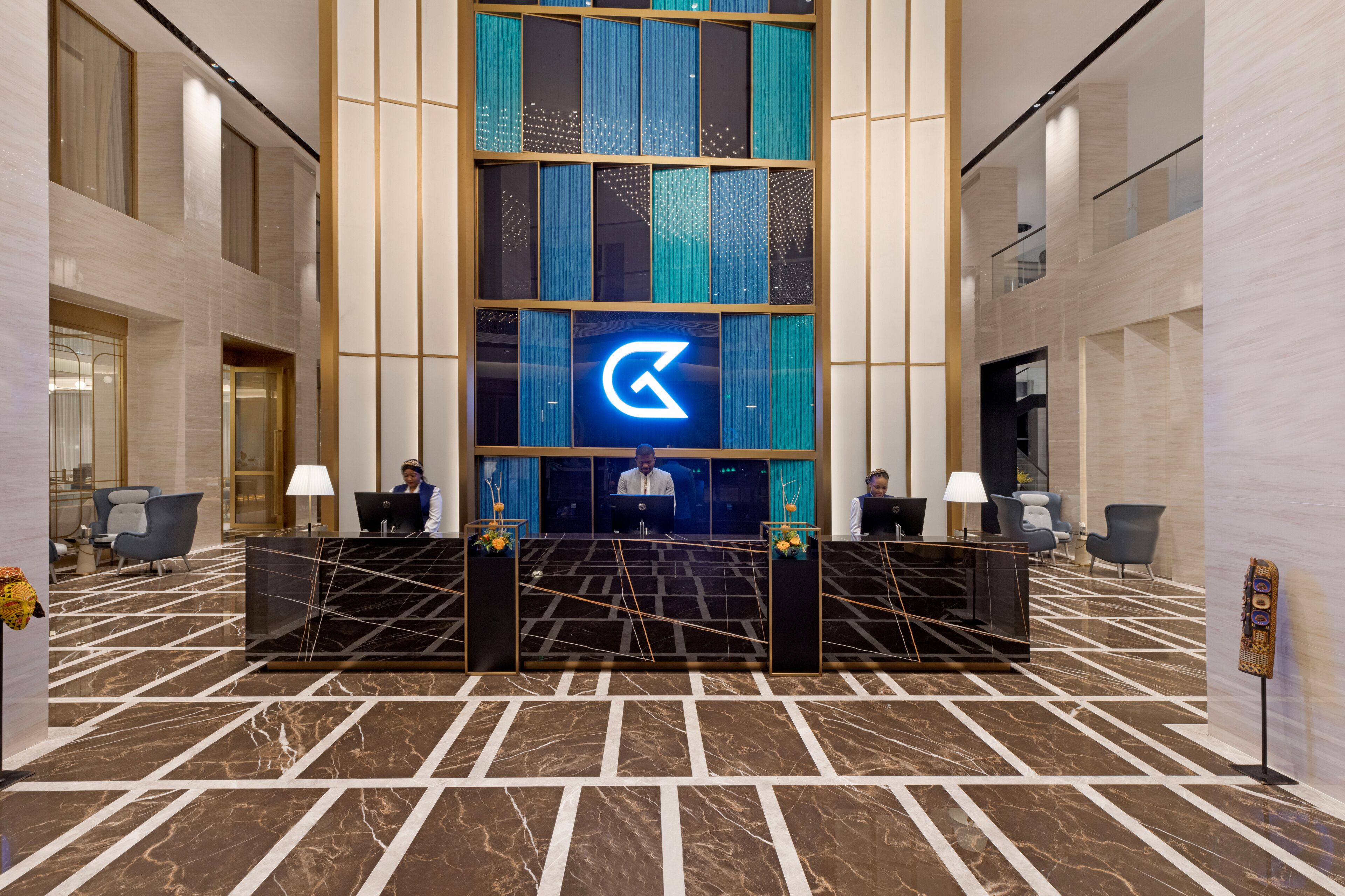 Un hall d’entrée moderne avec un comptoir d’accueil, deux réceptionnistes et un grand logo sur le mur.