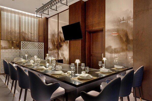 A long dining table set for a meal with chairs, a flat-screen TV mounted on the wall, and decorative wall panels. - Golden Tulip Kin-Oasis Kinshasa (Kinshasa)