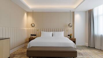 Habitación de hotel con una cama grande, un banco, dos mesitas de noche y una mesita con lámpara.