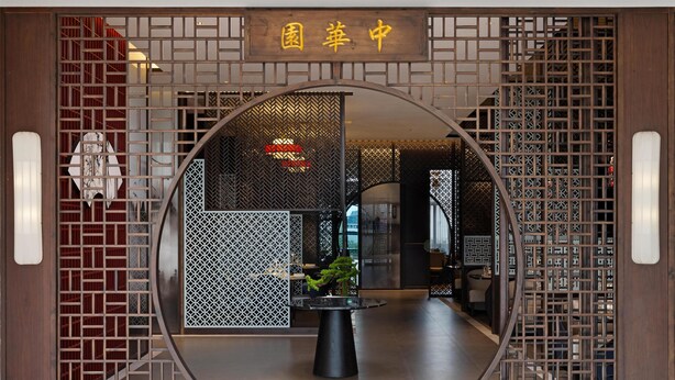 A traditional Chinese gate with a sign reading "Garden Center". Inside, there is a round table with a potted plant and a modern interior with wooden partitions and a visible staircase. - Golden Tulip Kin-Oasis Kinshasa (Kinshasa)