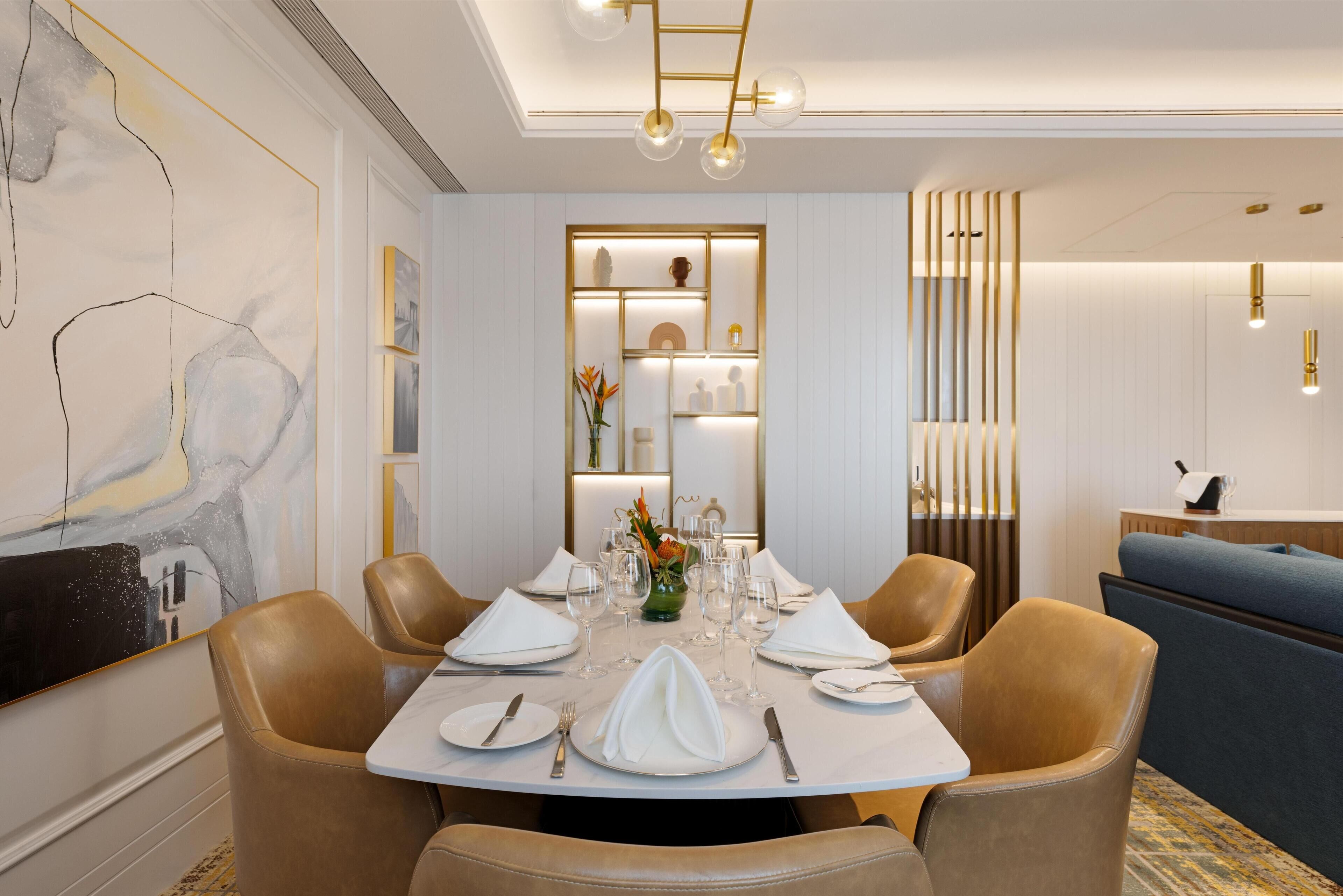 Un coin repas avec une table ronde dressée pour six personnes, entourée de fauteuils en cuir, et un lustre moderne au-dessus.