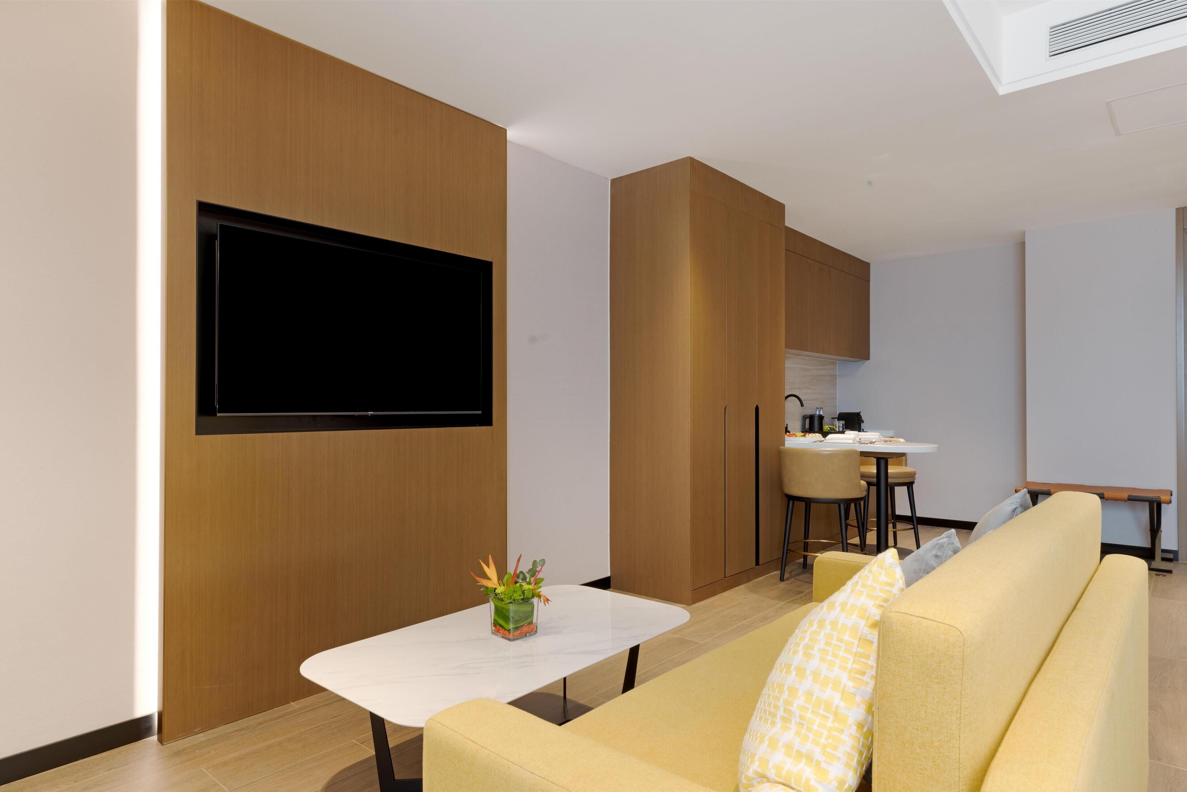 Ein modernes Wohnzimmer mit einem Flachbildfernseher, einem kleinen Tisch mit Pflanze und einem gelben Sofa.