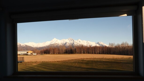 Ein Zimmer mit großem Fenster und Blick auf schneebedeckte Berge und ein Feld.