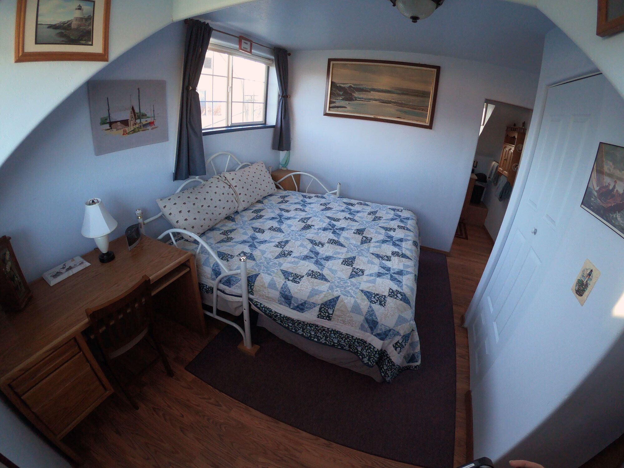 A bedroom with a bed, a desk, a chair, a window with curtains, and a painting on the wall.