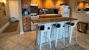 A kitchen with wooden cabinets, a stove, a microwave, and a refrigerator. There are four white bar stools around a central island. - Cozy studio in wonderful New Smyrna Beach walking distance to 27th ramp and park (New Smyrna Beach)