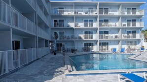 A multi-story hotel with a swimming pool, outdoor seating, and a clear sky. - Cozy studio in wonderful New Smyrna Beach walking distance to 27th ramp and park (New Smyrna Beach)