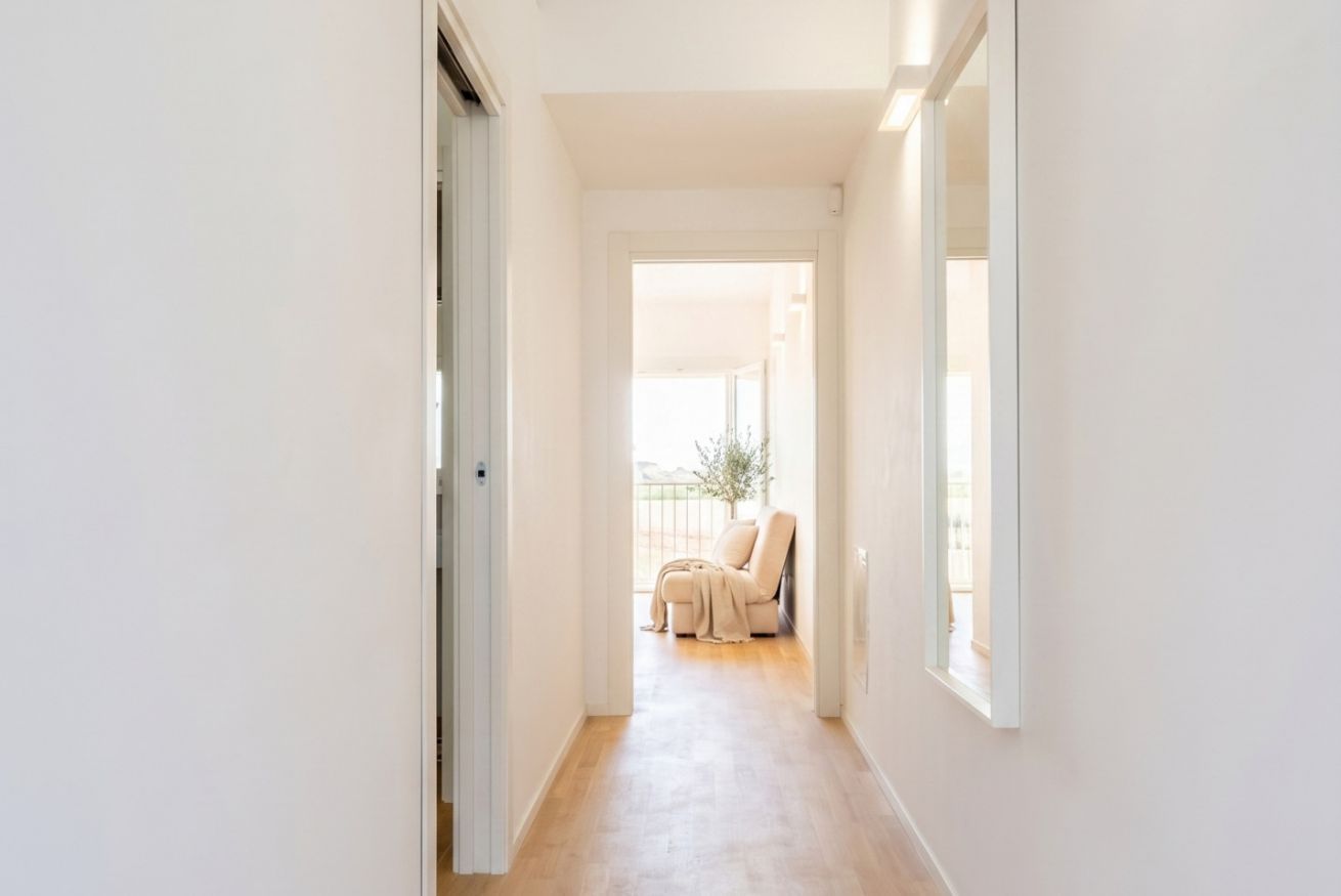 Un pasillo estrecho con piso de color claro, una puerta a la izquierda y una ventana a la derecha.