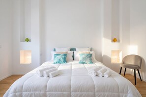 Una habitación de hotel con una cama grande, dos mesitas de noche, una silla y un ventanal pequeño.