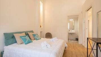 Ein Schlafzimmer mit Bett, Kissen, einem Sessel, einem Tisch und einem Badezimmer im Hintergrund.