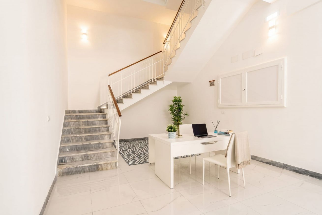 Un intérieur moderne avec un escalier, un bureau avec un ordinateur portable et une plante en pot.