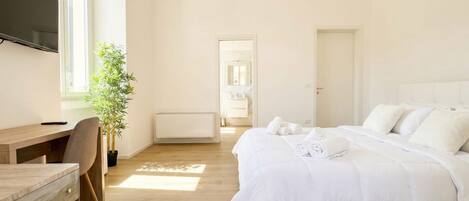 A bedroom with a bed, a desk, a chair, a potted plant, and a TV.