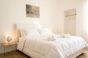 A neatly made bed with white bedding and rolled towels, a bedside lamp, and a painting on the wall.