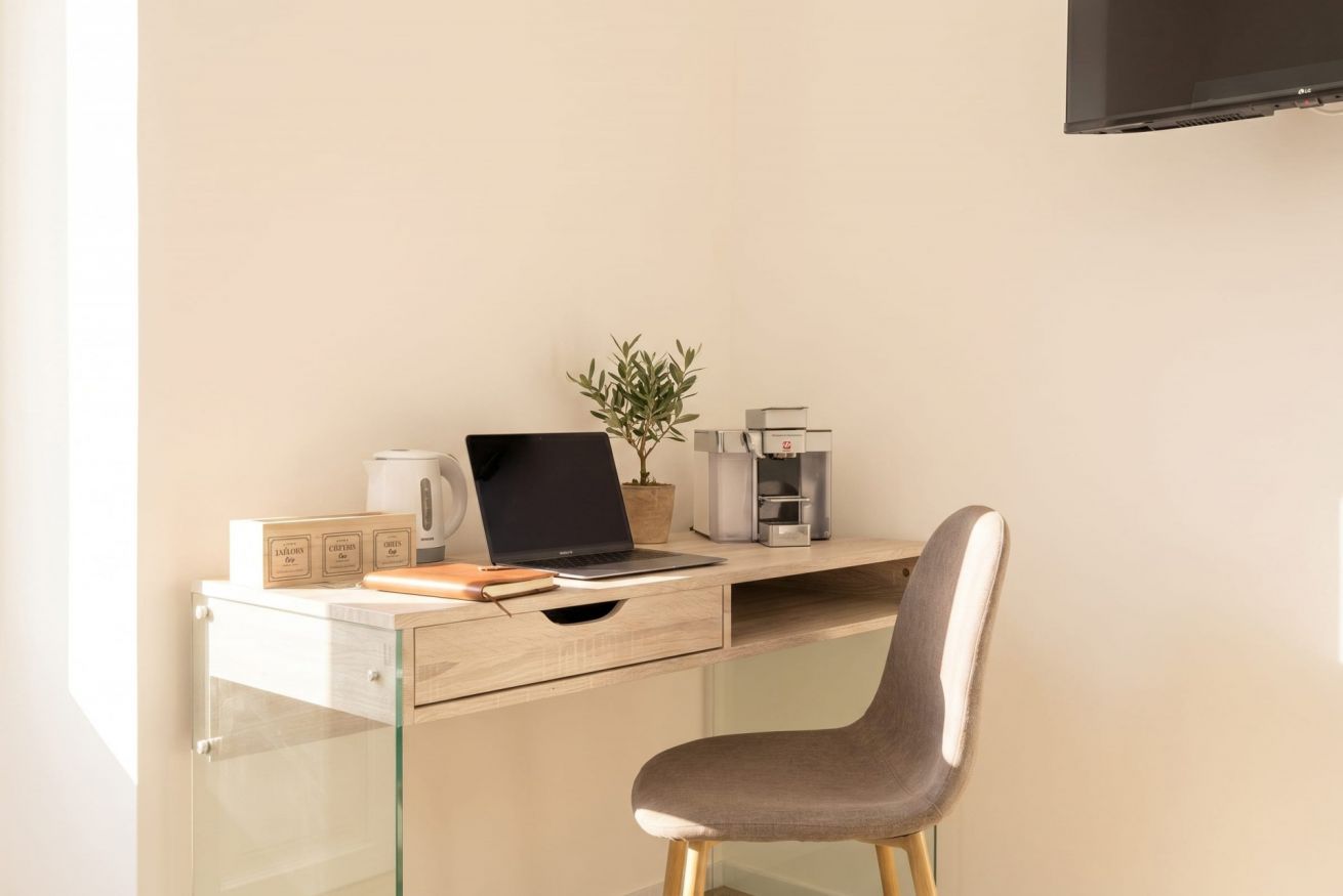 Un espace de travail moderne comprenant un ordinateur portable, une plante en pot, une machine à café et une lampe de bureau.