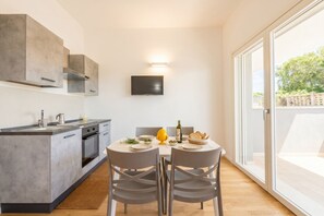A modern kitchen with a dining area, a flat-screen TV mounted on the wall, and a sliding glass door leading to an outdoor area. - Benjamin House with Private Parking (Bari)