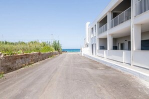 A coastal road leading to a white building with balconies overlooking the sea.