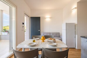A modern kitchen with a dining area, a grey sofa, and a view of greenery outside.