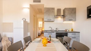 Une cuisine moderne avec des meubles gris, un four encastré et un coin repas comprenant une table et des chaises blanches.