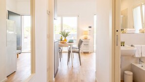Une chambre d’hôtel moderne avec un plancher en bois, un coin repas comprenant une table et des chaises, un coin cuisine et une salle de bain avec un lavabo et un miroir.