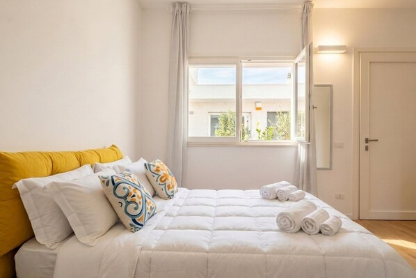 A bedroom with a bed, pillows, a window, and a door.