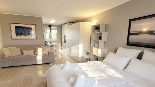 A modern hotel room with a large bed, a sofa, a desk, and a view of the room's interior.