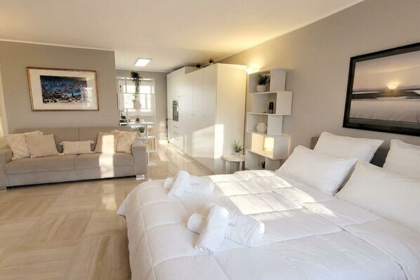 A modern hotel room with a large bed, a sofa, a desk, and a view of the room's interior.