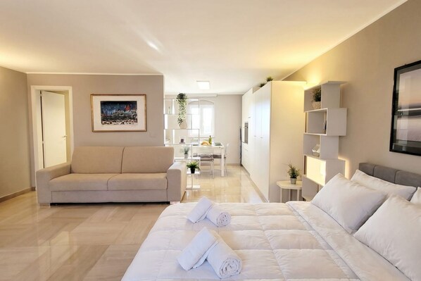 A modern hotel room with a bed, a sofa, a dining area, and a kitchen.