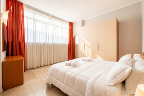 A hotel room with a bed, a wardrobe, a desk, and a window with curtains.