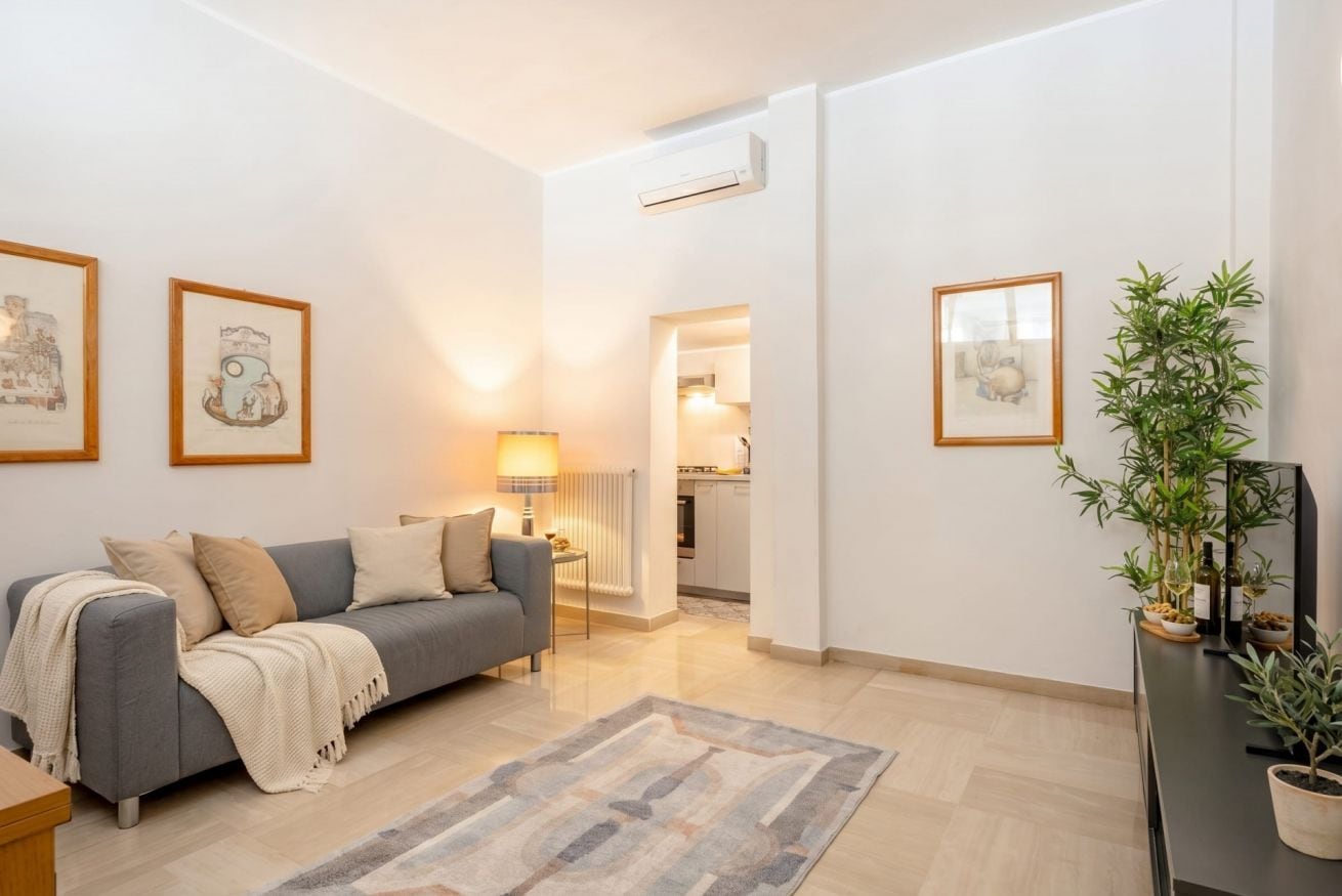 Een moderne woonkamer met een grijze bank, een salontafel, een lamp en lijstwerken aan de muren.