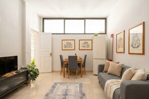 A modern living room with a sofa, TV, dining table, and artwork on the walls.