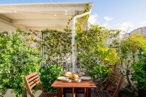 An outdoor dining area with a table set for two, surrounded by lush greenery and a white lattice fence.