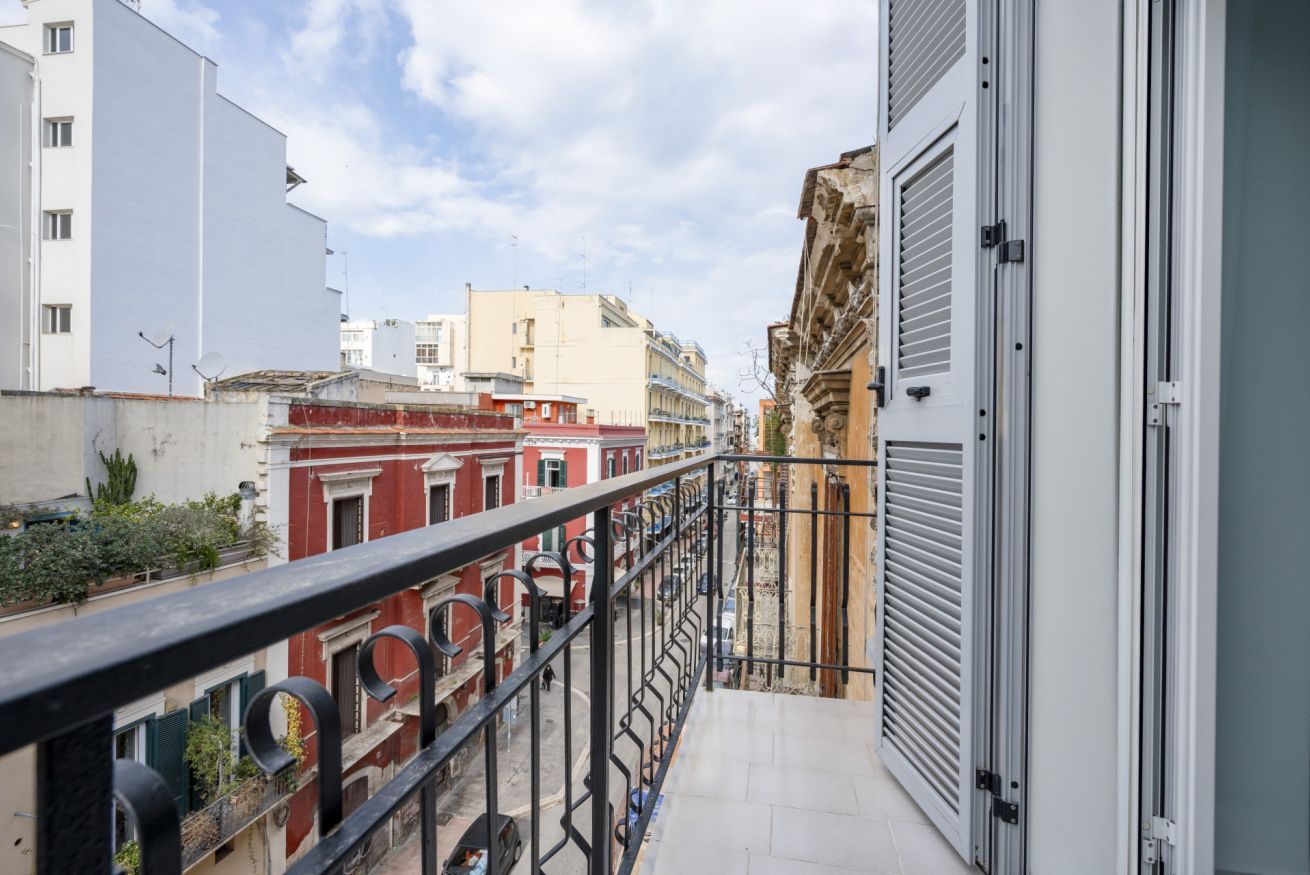 Ein Balkon mit Metallgeländer, der auf eine Straße mit Häusern blickt.