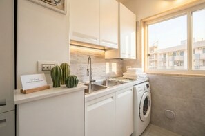 A modern kitchen with a built-in washing machine, a sink, and a window with a view of buildings.