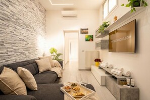 A modern living room with a grey sofa, a tray with snacks and glasses, a TV on the wall, and a plant.