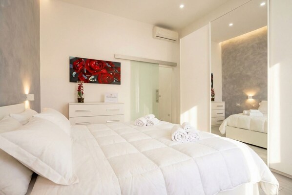 A modern bedroom with a large bed, a dresser, a mirror, and a painting on the wall.