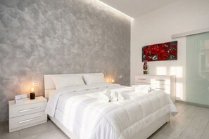 A modern bedroom with a large bed, bedside tables, a painting, and a nightstand with a lamp. - Casa di Carly - large cozy retreat in center (Bari)
